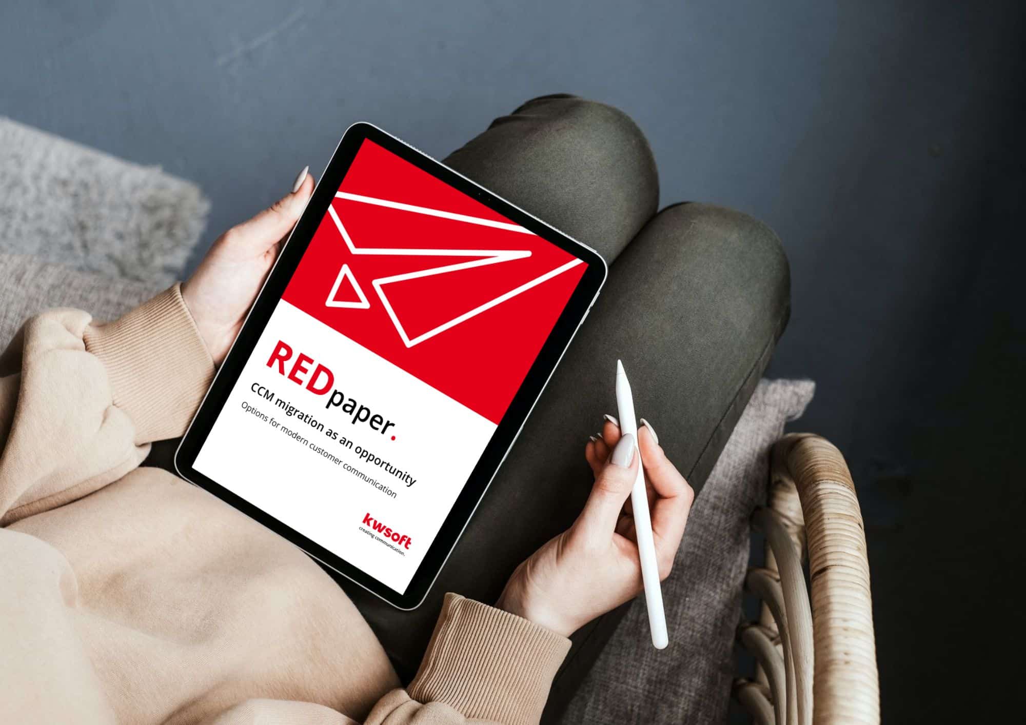 Obrázek ukazuje tablet, který drží někdo v ruce, a na něm je obálka REDpaper „CCM Migration“.